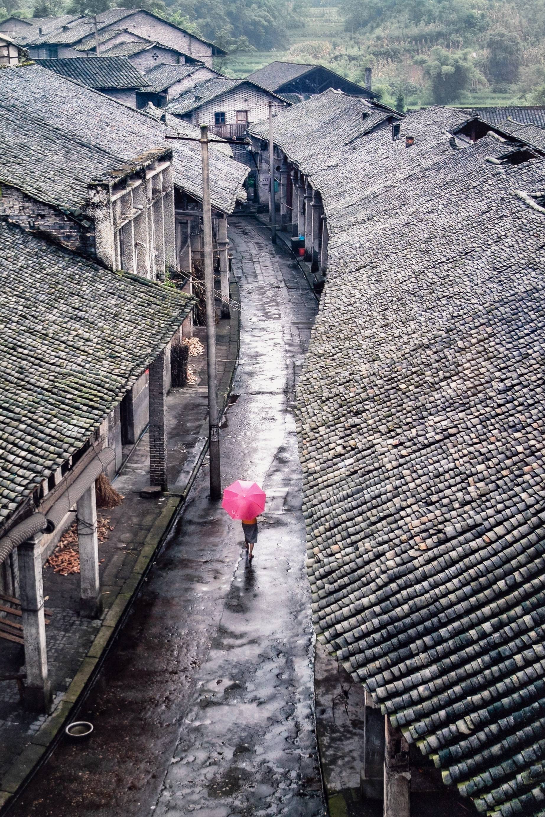 small village street with figure walking down the road holding an umbrella